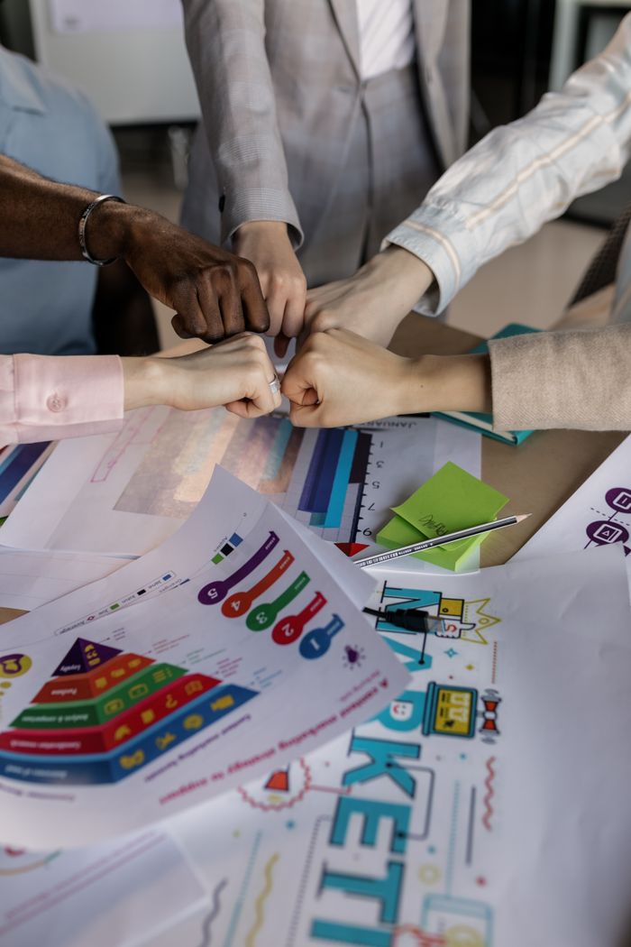 services-01 A group collaborates with a fist bump over colorful marketing charts, showcasing teamwork.